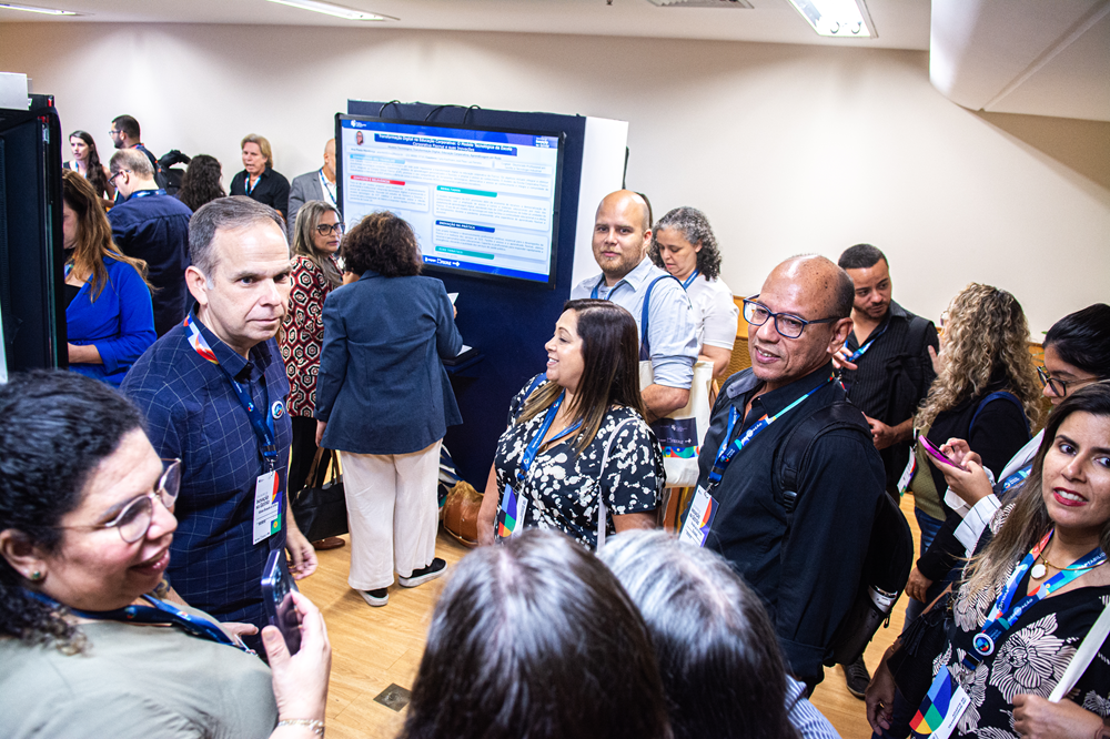 Imagem mostra trabalhadores em pé conversando, em meio à exposição de trabalhos acadêmicos